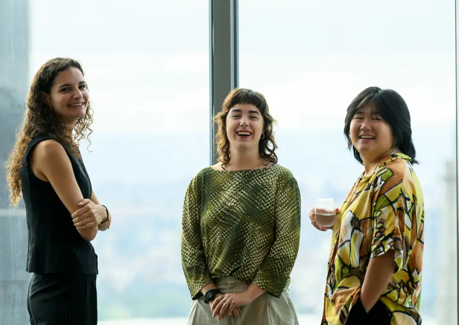 Three attendees talking over coffee before the programme, the city behind them.